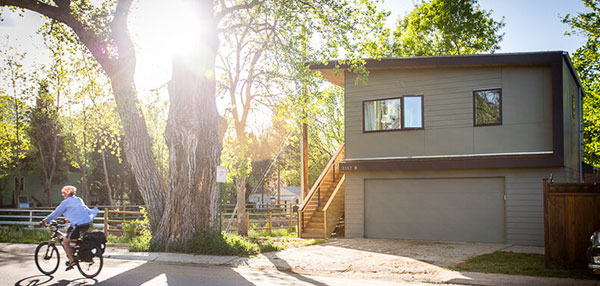 A person rides a bicycle past an accessory dwelling unit on a sunny day.