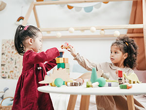 Two toddler girls playing with blocks at a table.