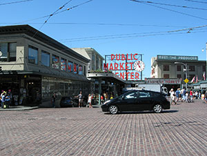 A car drives by Pike Place Market on a street that covers drainage pipes.