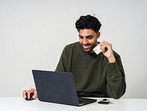 A man smiling while paying a bill using a credit card and a laptop.