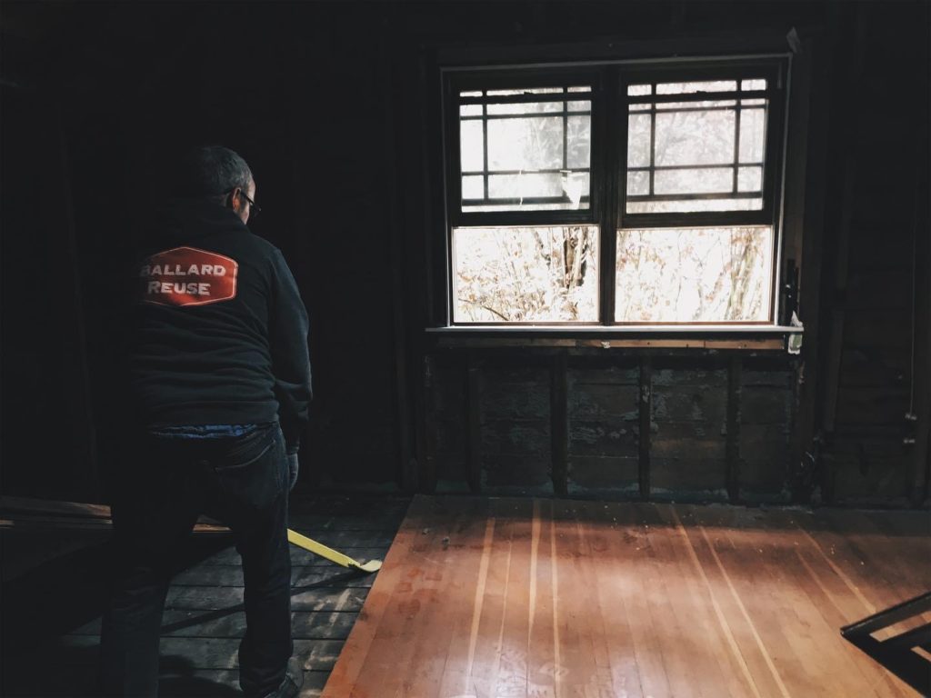 A man from a salvaging company prying up fir floor boards to salvage them.