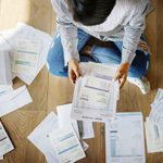 A woman sitting on the floor looking at several invoices that need to be paid.